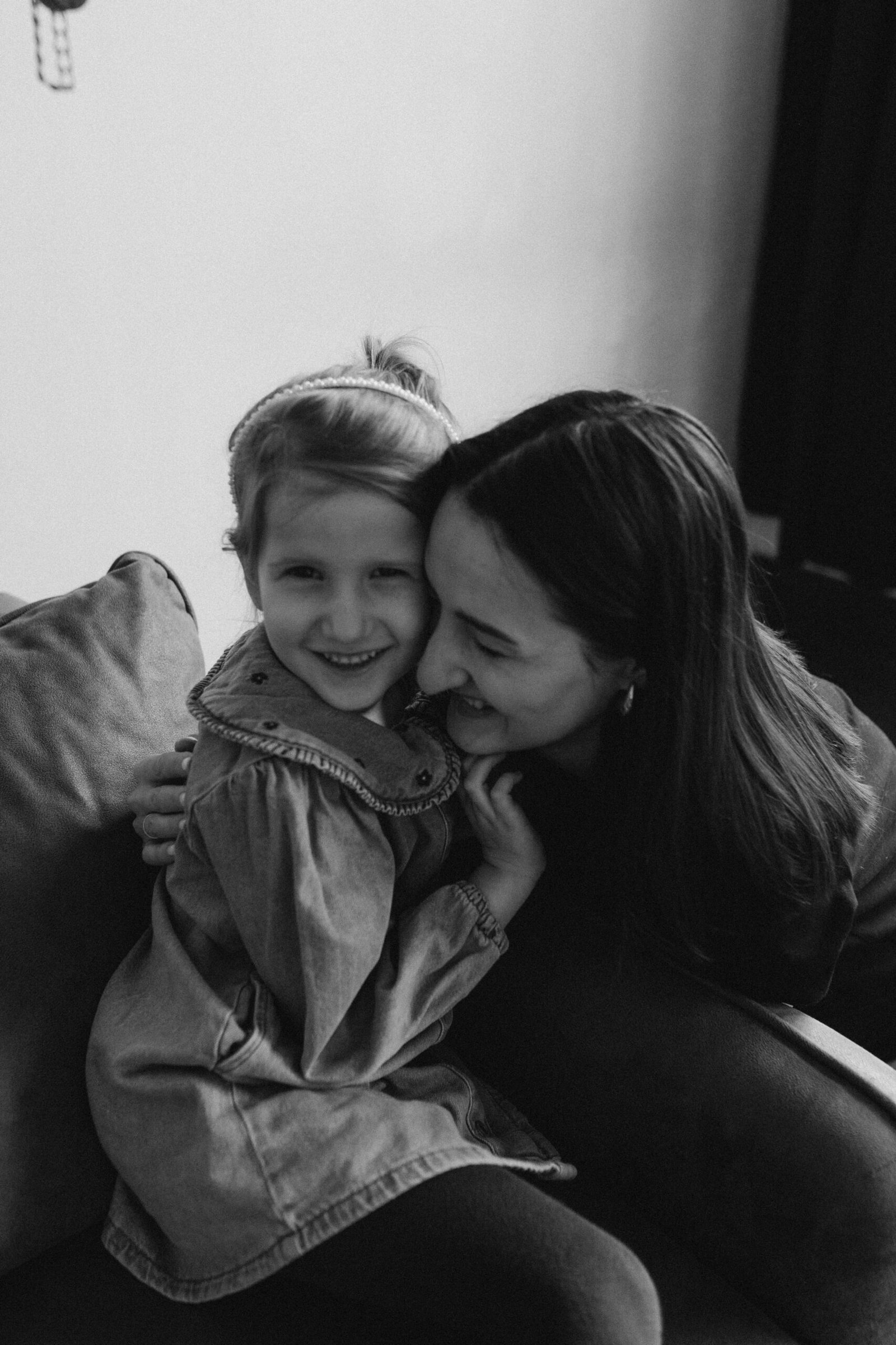 A joyful black and white moment of mother and daughter sharing a happy embrace indoors.